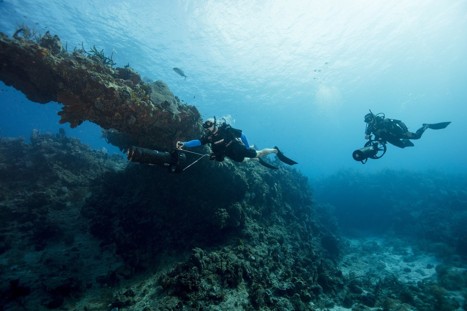 Divers with scooters along a reef wall