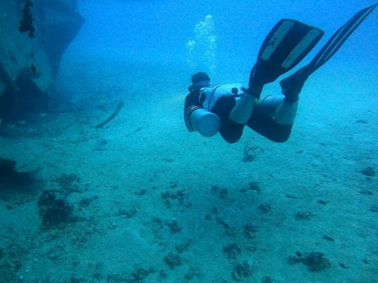 A sidemount diver gliding over the sand in clear blue water