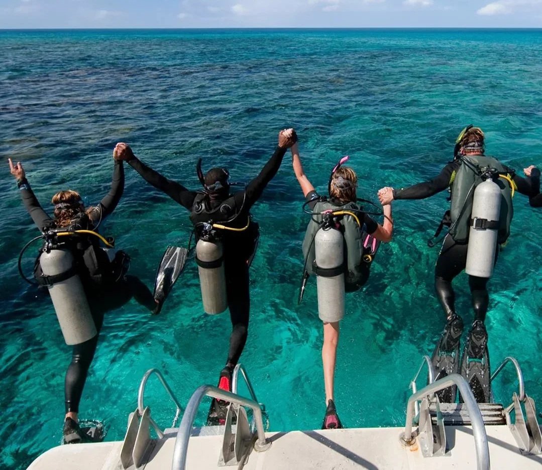 New divers holding hands underwater over a sandy reef